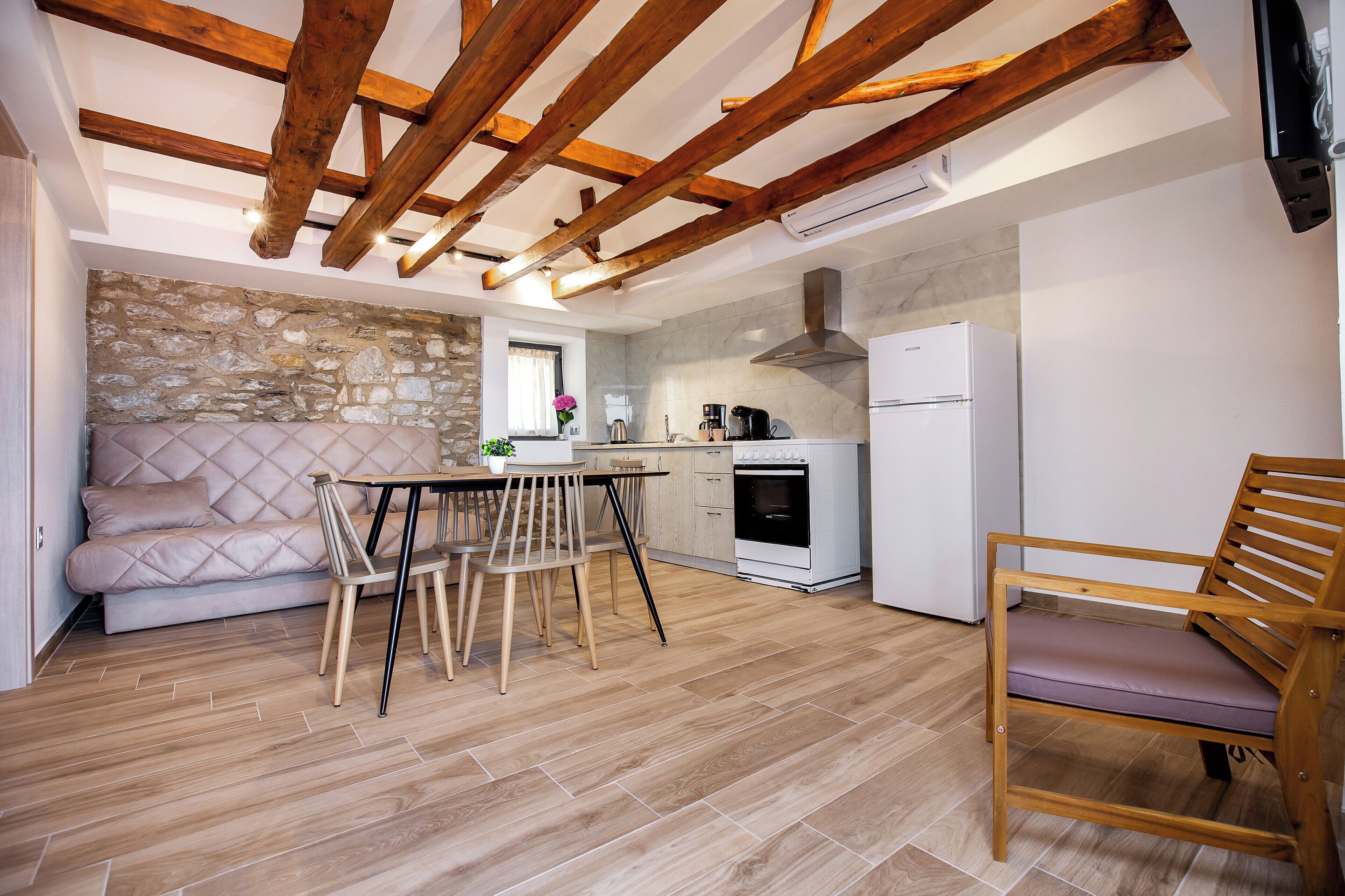 Una cocina acogedora con vigas de madera a la vista, una pared de piedra, un sofá, una mesa de comedor con sillas y un banco de madera.