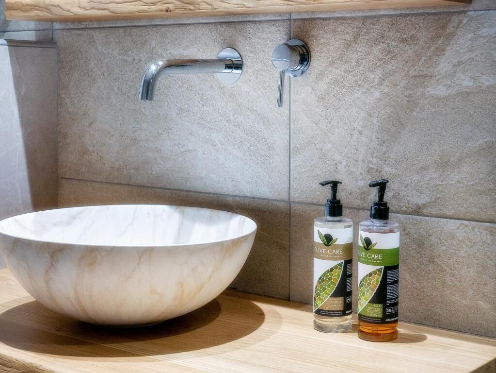A bathroom with a large marble sink, two olive care shampoo bottles, and a faucet.