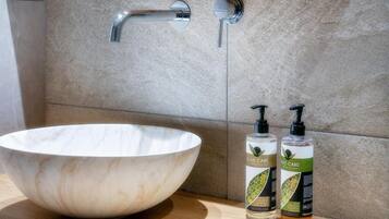 Une salle de bain avec un grand lavabo en marbre, deux flacons de shampoing pour les cheveux, et un robinet.