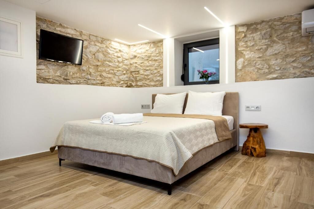 A bedroom with a stone wall, a flat-screen TV, a bed with a beige bedspread, and a window with a view.