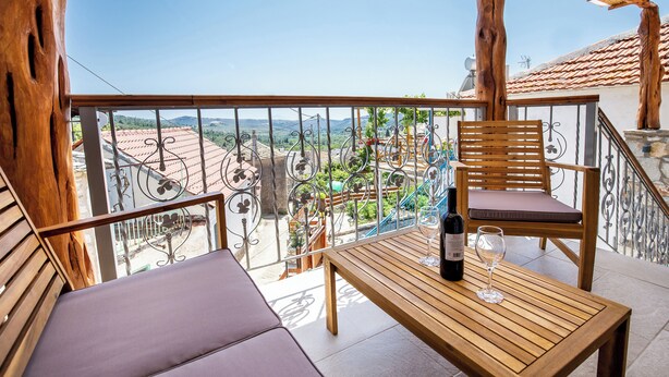A balcony with a wooden table, a chair, and a bottle of wine. - Theros Easy Living (Thasos)