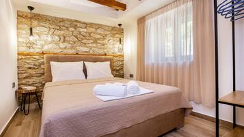 A bedroom with a stone wall, a wooden headboard, a bed with a beige quilt, a small bedside table, and a hanging light fixture.