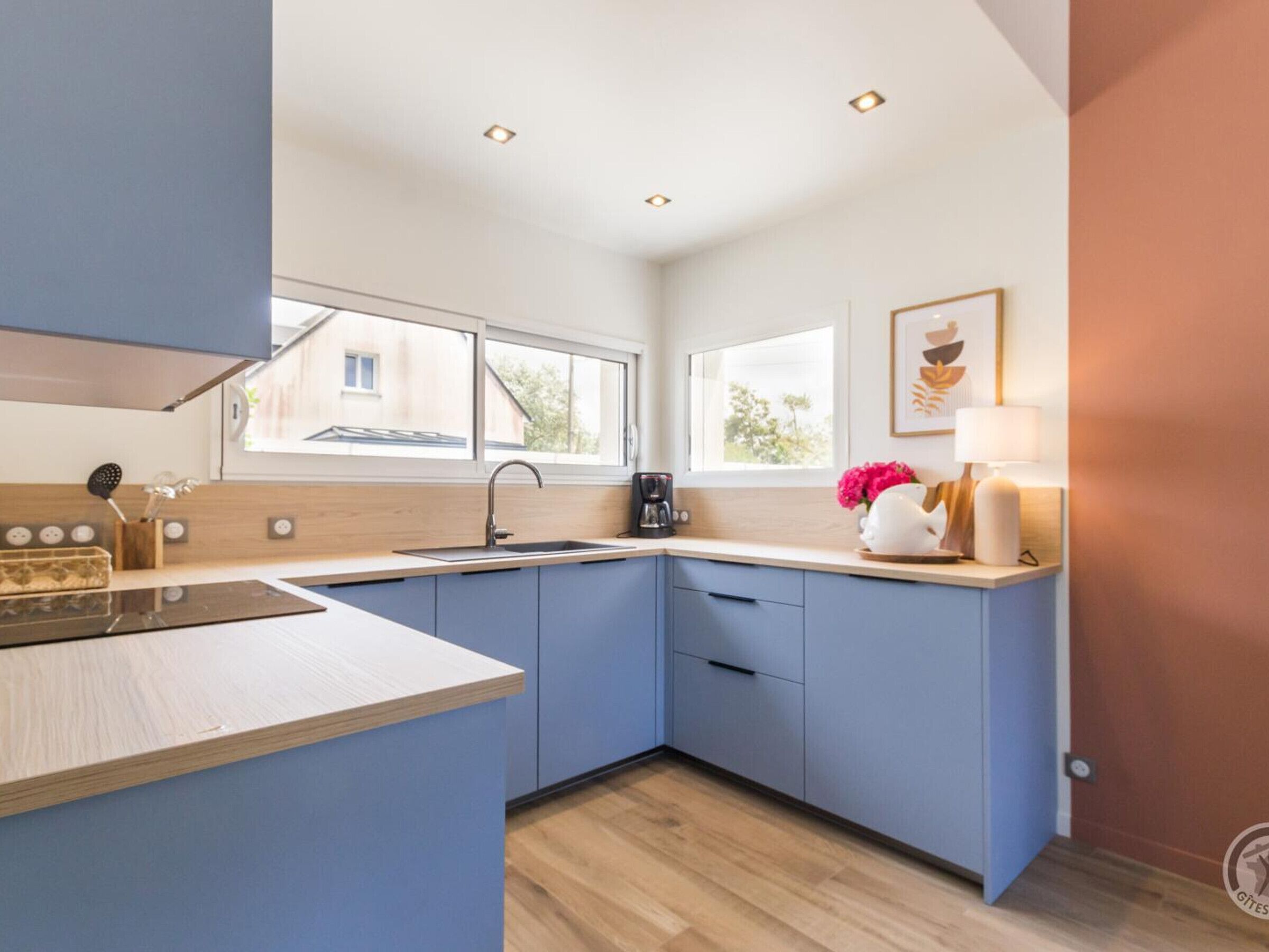 A modern kitchen with blue cabinets, a wooden countertop, a sink, and a window providing natural light.