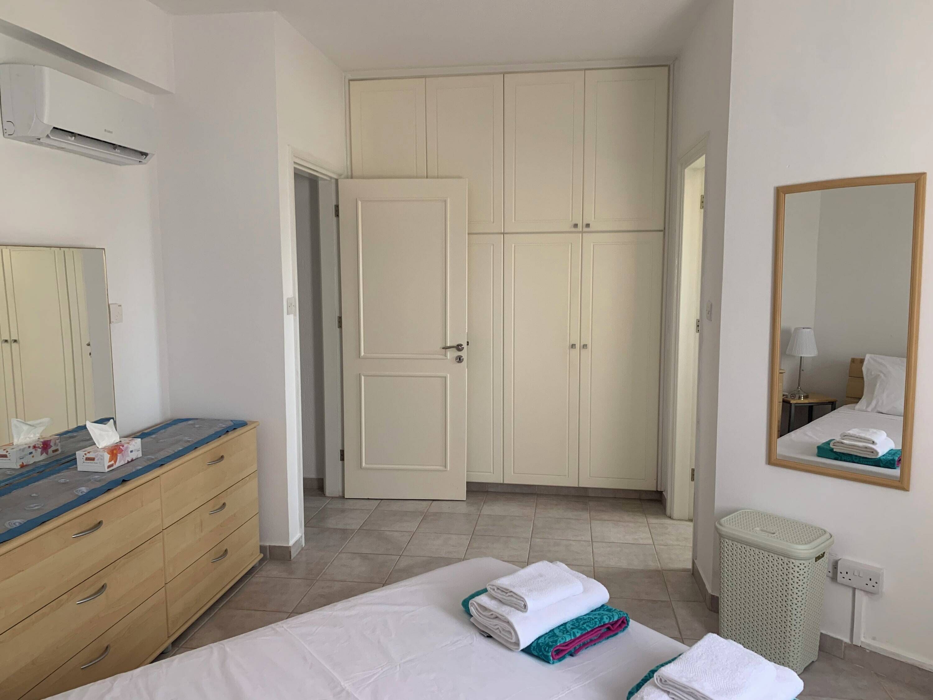 Habitació d'hotel amb un llit, un taulell de nit de fusta, un armari, un mirall i un gresol.