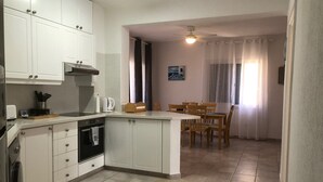 Une cuisine compacte avec des meubles blancs, un four encastré et un coin repas comprenant une table et des chaises.