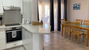 Une cuisine moderne avec des meubles blancs, un four encastré et une machine à café. On y trouve également un coin repas avec une table et des chaises en bois.