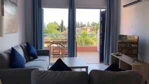 Una sala de estar con sofá, televisión y un balcón con mesa y sillas.