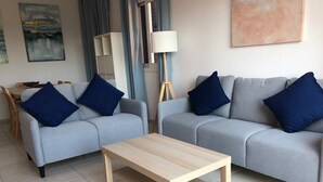 Una sala de estar con dos sofás grises, cada uno con una almohada azul, una mesa de centro de madera y una lámpara de pie.