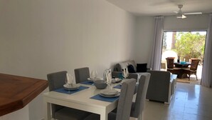 Ein Essbereich mit einem weißen Tisch, gedeckt für vier Personen, grauen Polsterstühlen und einem grauen Sofa im Hintergrund.