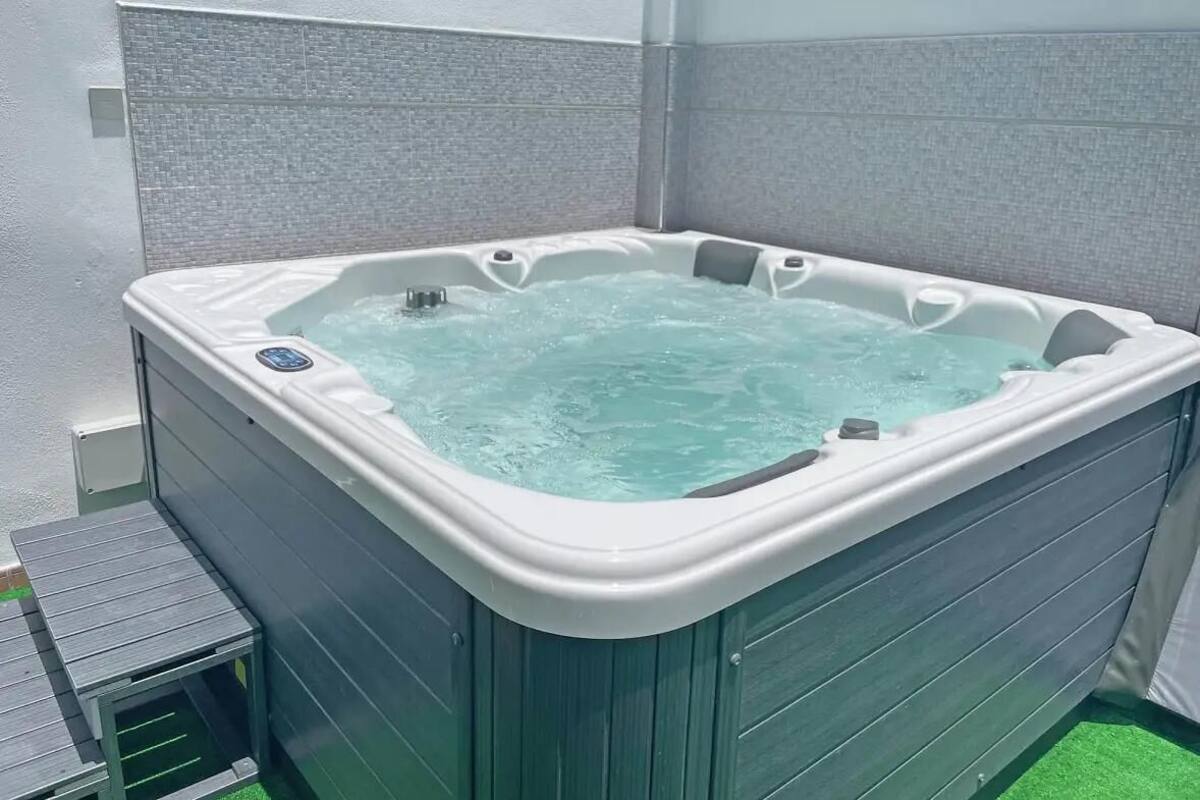 A hot tub with a tiled surround, a wooden deck, and a green artificial turf area.