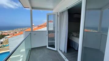 A balcony with a glass door leading to a bedroom with a bed and a view of the sea.