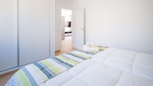 A modern bedroom with a large bed, a wardrobe, and a bathroom visible through an open door. - Moderno Apartamento en Corralejo (La Oliva)