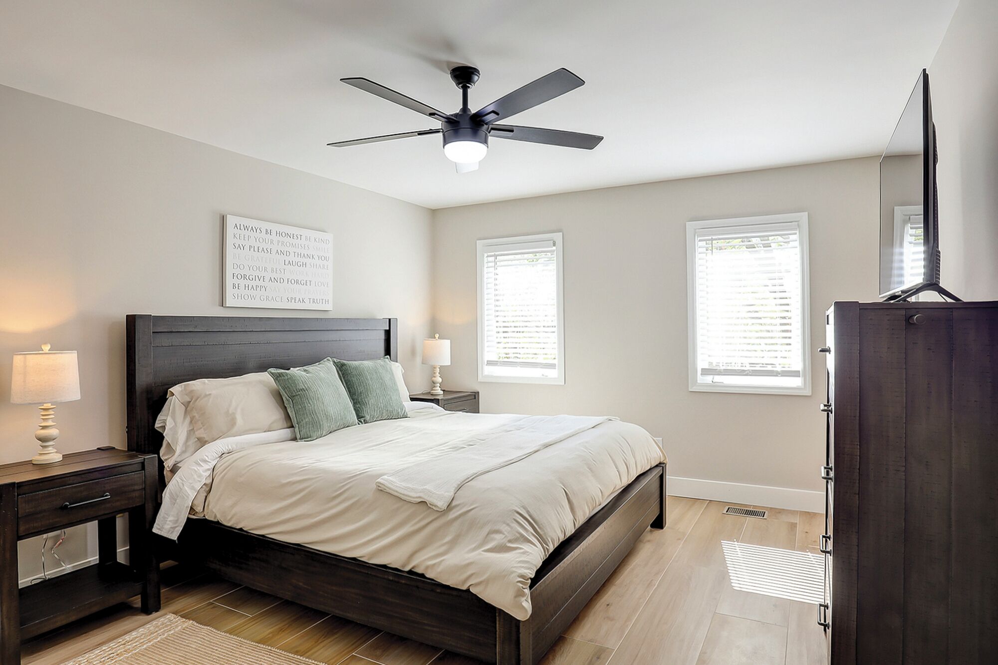 A bedroom with a bed, nightstands, a ceiling fan, a window, and a wardrobe.