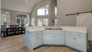 A spacious kitchen with a large island, light blue cabinets, and a view of the outdoors through large windows. - Double Master Suite Luxury 4 BR Sea Pines Home, Bikes & Beach Gear included (Hilton Head)