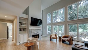 A spacious living room with a fireplace, large windows, and a television. - Double Master Suite Luxury 4 BR Sea Pines Home, Bikes & Beach Gear included (Hilton Head)
