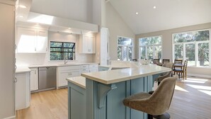 A spacious kitchen with white cabinetry, a large island, and a dining area with a view of palm trees. - Double Master Suite Luxury 4 BR Sea Pines Home, Bikes & Beach Gear included (Hilton Head)
