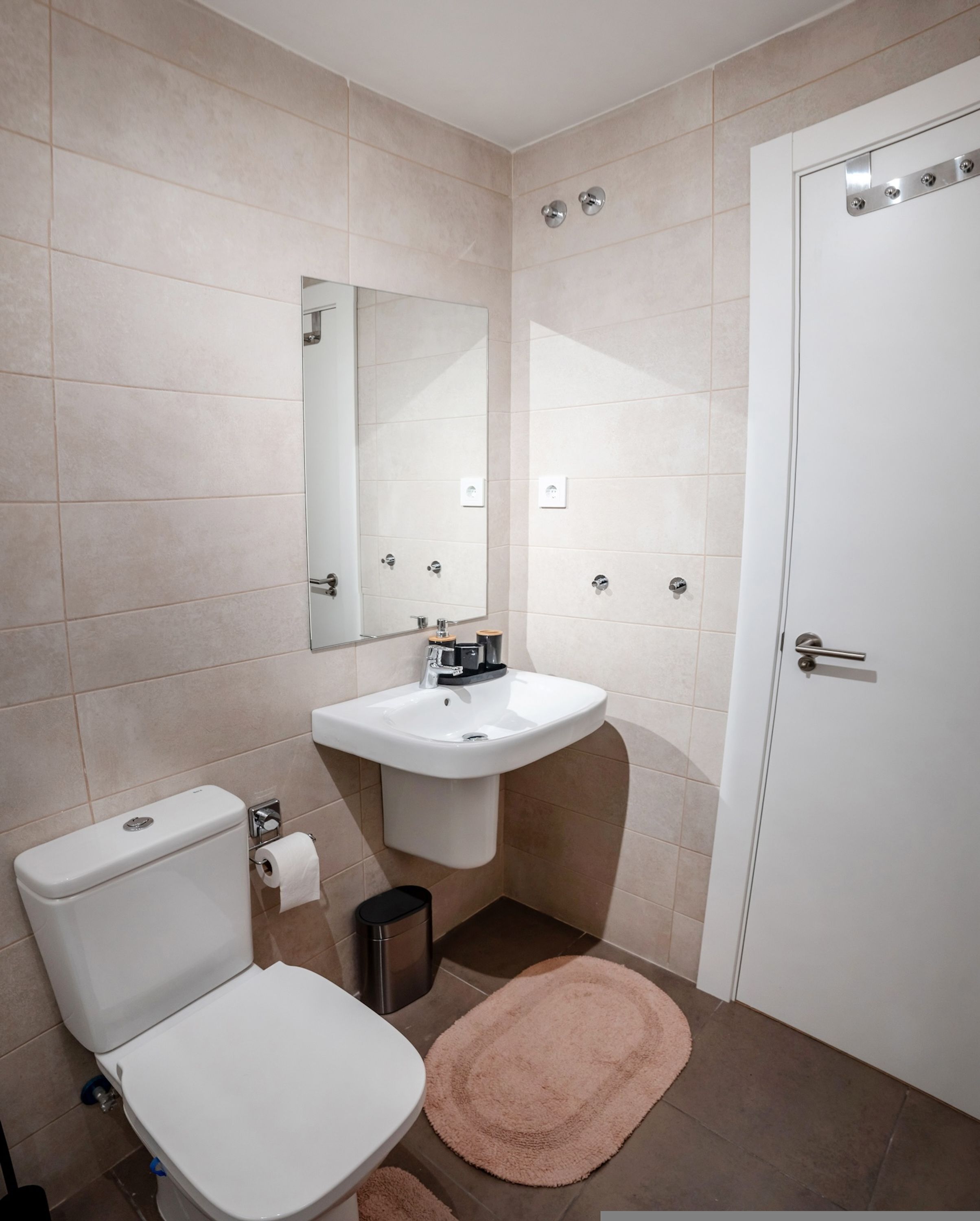 A bathroom with a toilet, sink, mirror, and a door.