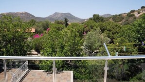 Vista desde un balcón con barandilla metálica, que da a un paisaje montañoso con árboles y edificios.