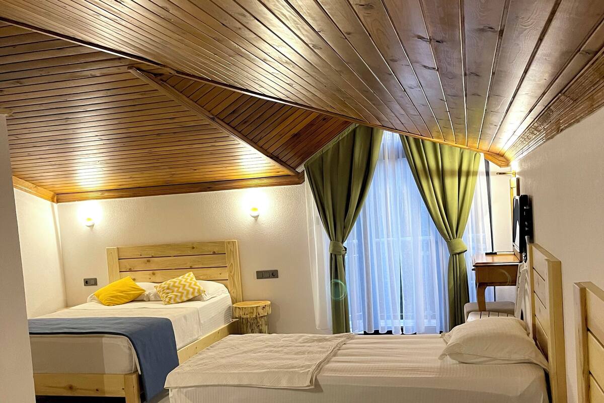 A room with three beds, wooden ceiling beams, and a window with curtains.