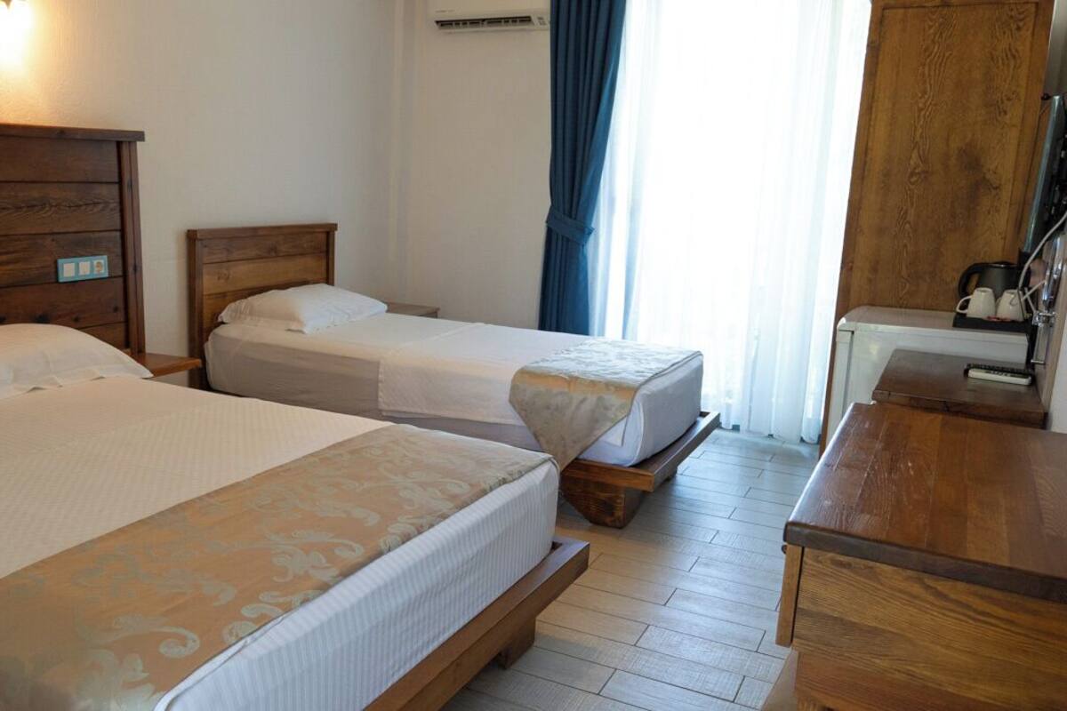 A hotel room with two beds, wooden headboards, a wooden dresser, and a window with curtains.