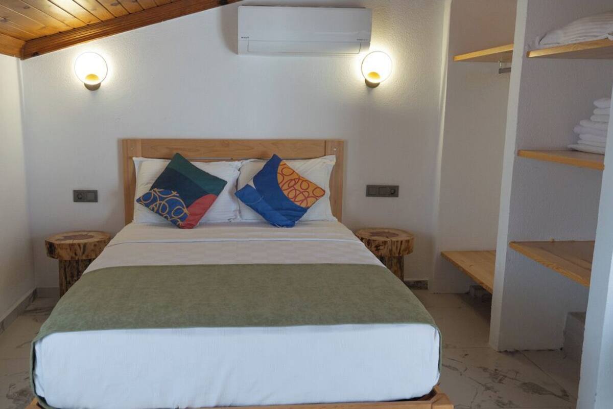 A bedroom with a bed, two bedside tables, a wooden headboard, a shelf with folded towels, and an air conditioning unit.