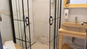 Un baño con cabina de ducha de vidrio, un lavabo color beige y pared con azulejos de mármol.