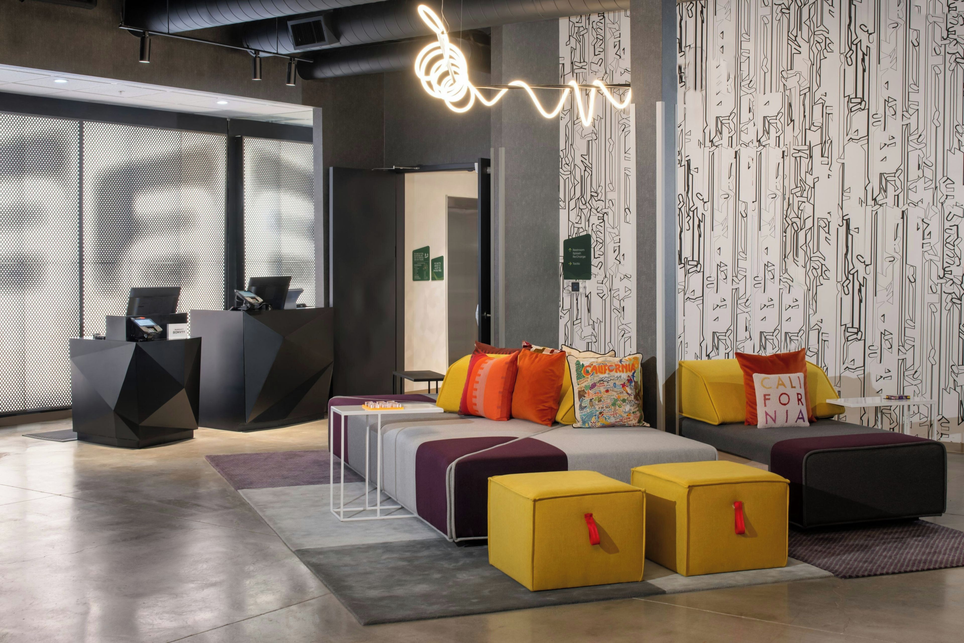 Un interior moderno con mostrador de recepción, zona de estar con cojines coloridos y una pared con estampado.