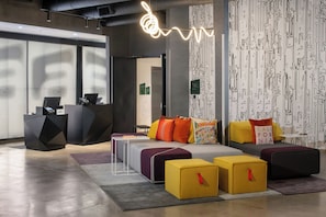 Un interior moderno con mostrador de recepción, zona de estar con cojines coloridos y una pared con estampado.