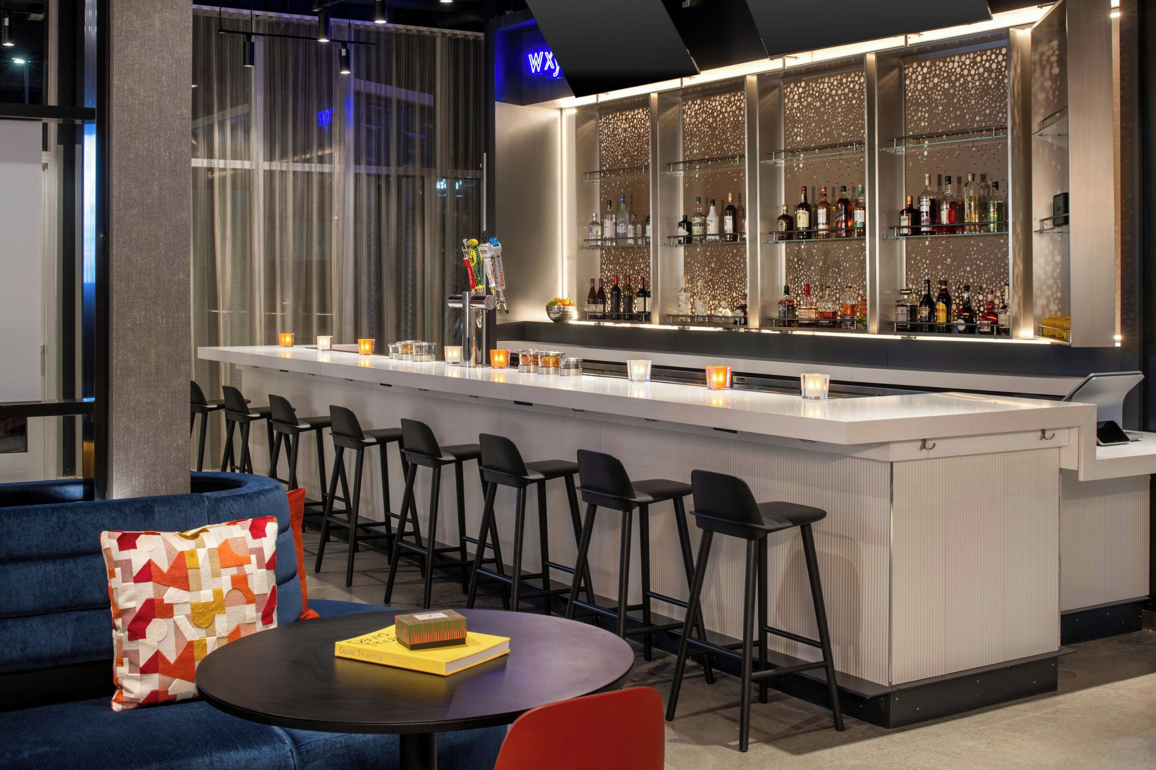 Un espace bar doté d’un comptoir blanc, de tabourets de bar et d’une variété de bouteilles et de verres.