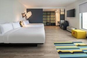Una habitación de hotel moderna con una cama grande, un televisor de pantalla plana, un escritorio pequeño y un espacio de almacenamiento.