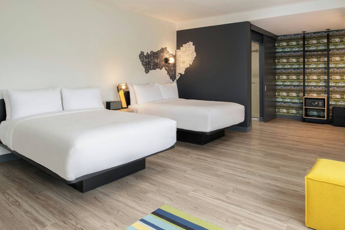 Een moderne hotelkamer met twee bedden, een houten vloer, wanddecoratie met een kaart en een boekenkast met ingelijste foto's.