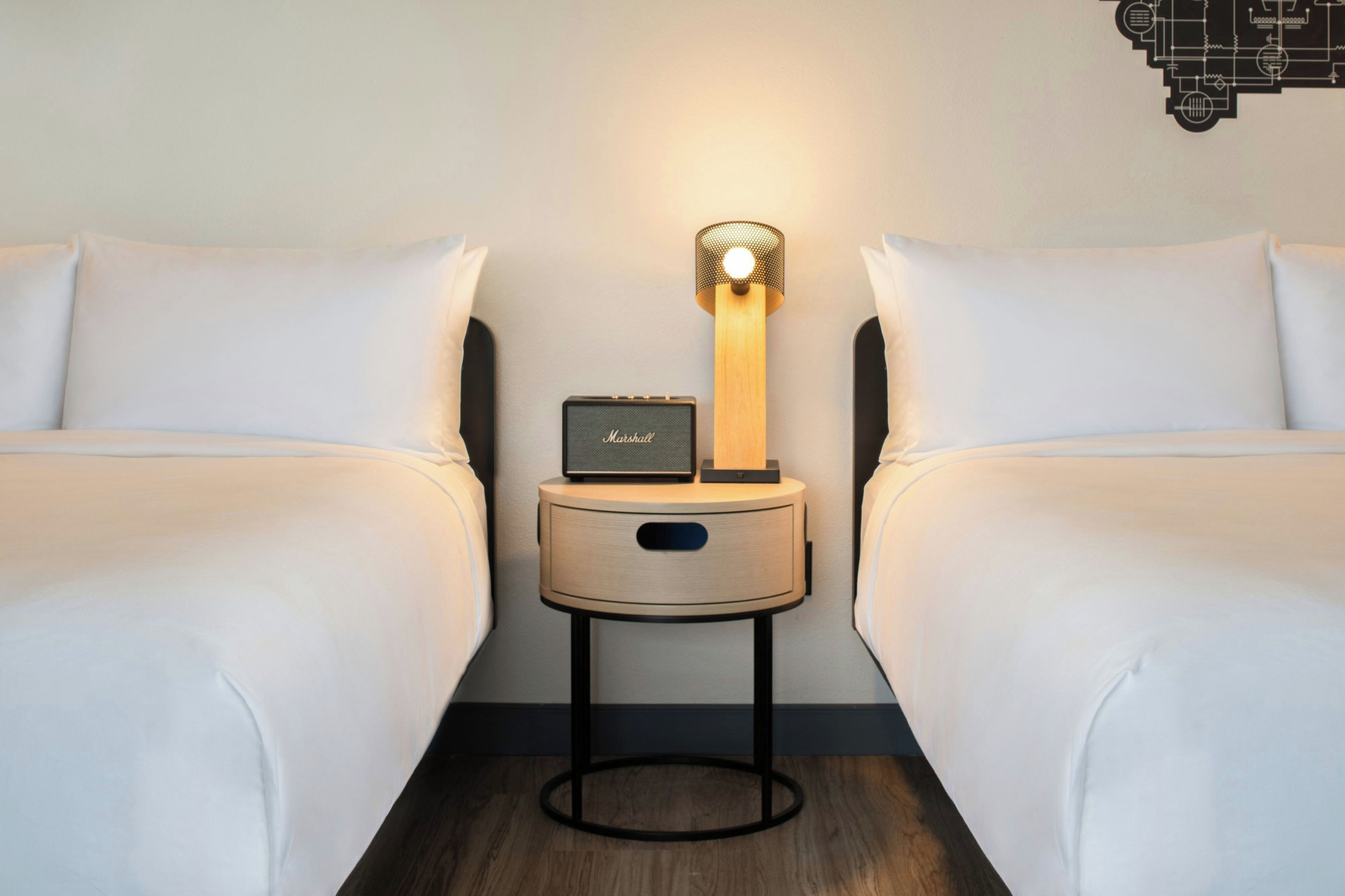 A hotel room with two single beds, a nightstand with a lamp, and a small table.