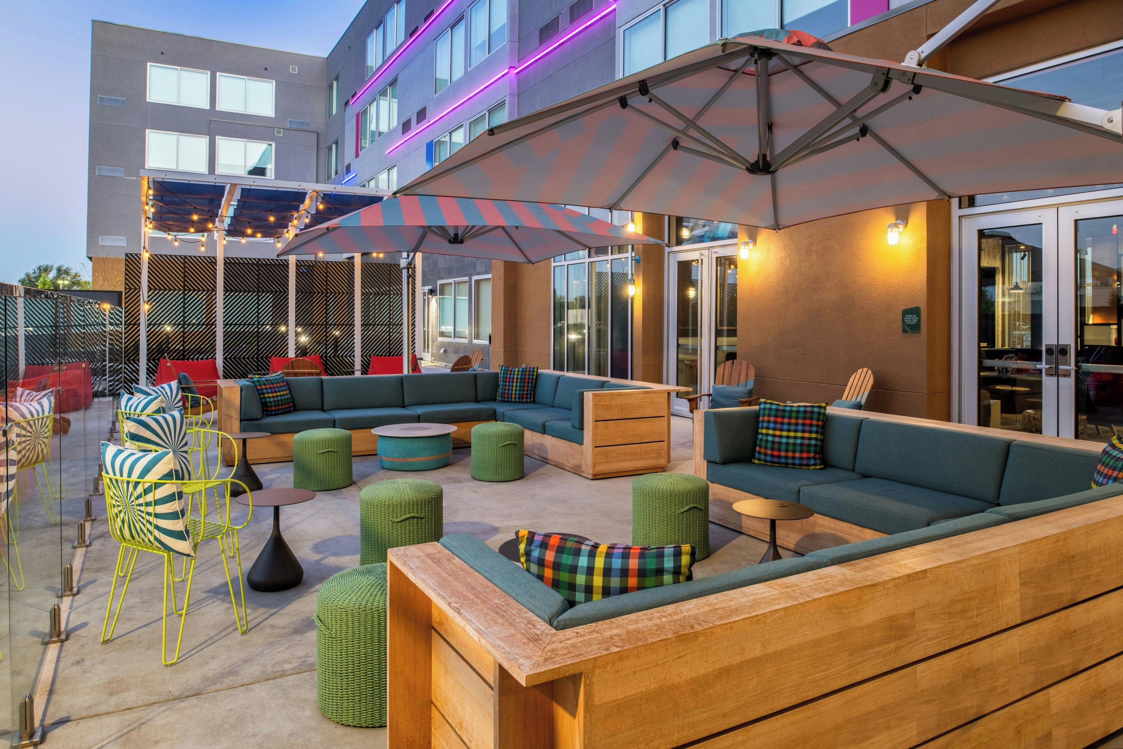 An outdoor seating area with sofas, ottomans, and tables, and a building with large windows and a modern design.