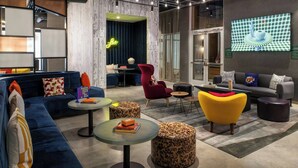 Un área de estar moderna con sofás, sillones y mesas redondas, que presenta un letrero de neón y una exhibición de arte digital.