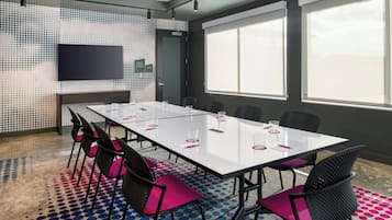 Ein Konferenzraum mit langem Tisch, Stühlen, einem Flachbildfernseher und großen Fenstern.