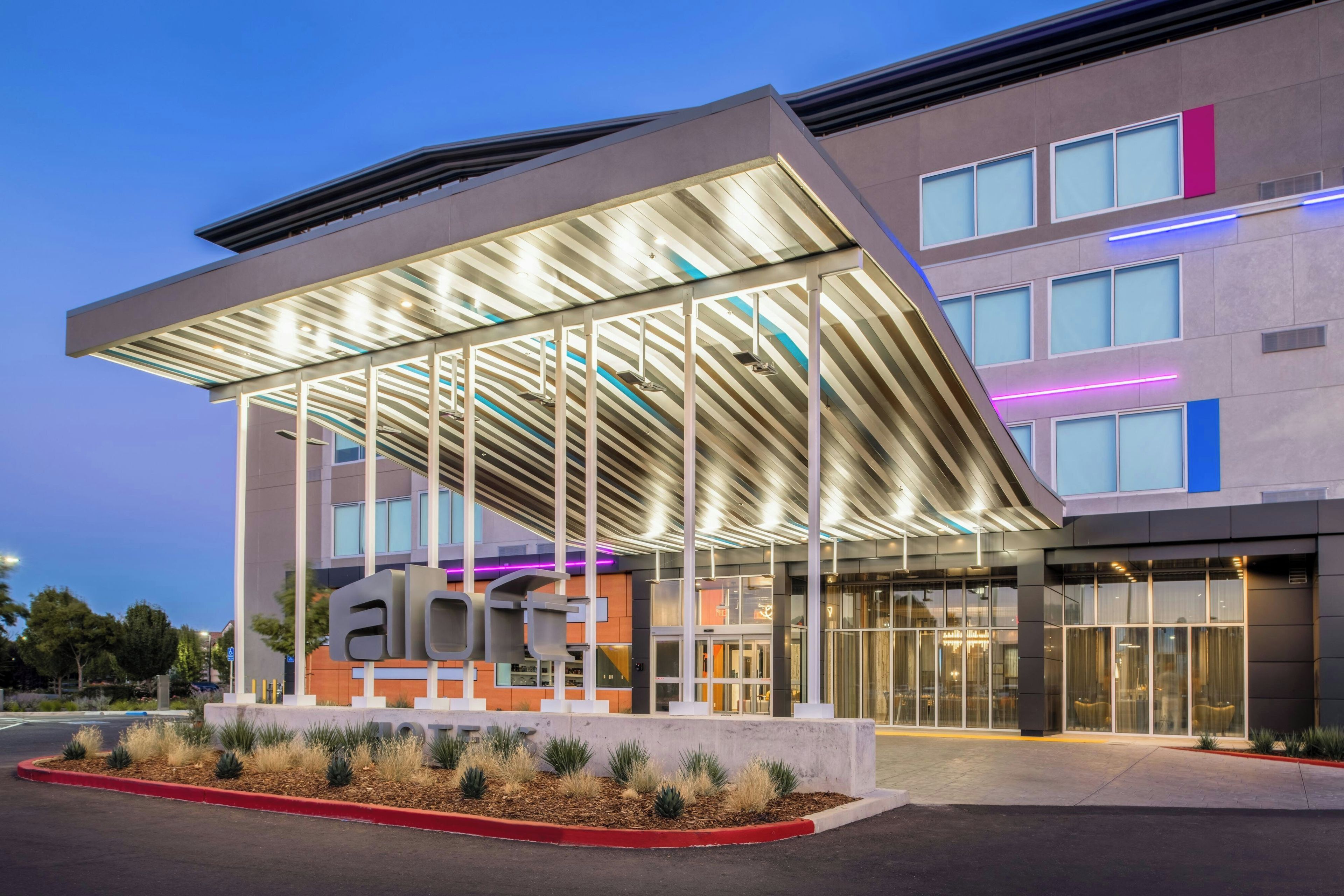 A modern building with a covered entrance, large windows, and a sign with the word 'hotel'.