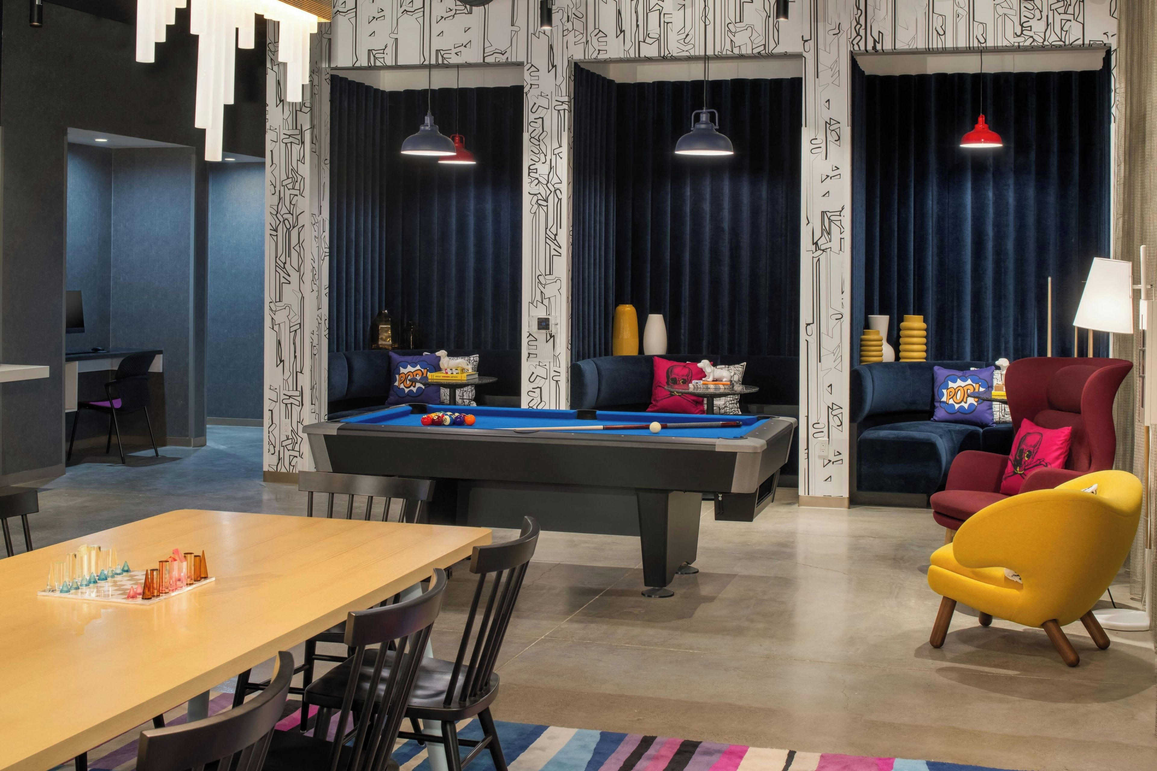 A modern living room with a pool table, a sofa, a yellow armchair, and a dining area with chairs and a table.