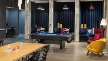 A modern living room with a pool table, a sofa, a yellow armchair, and a dining area with chairs and a table.