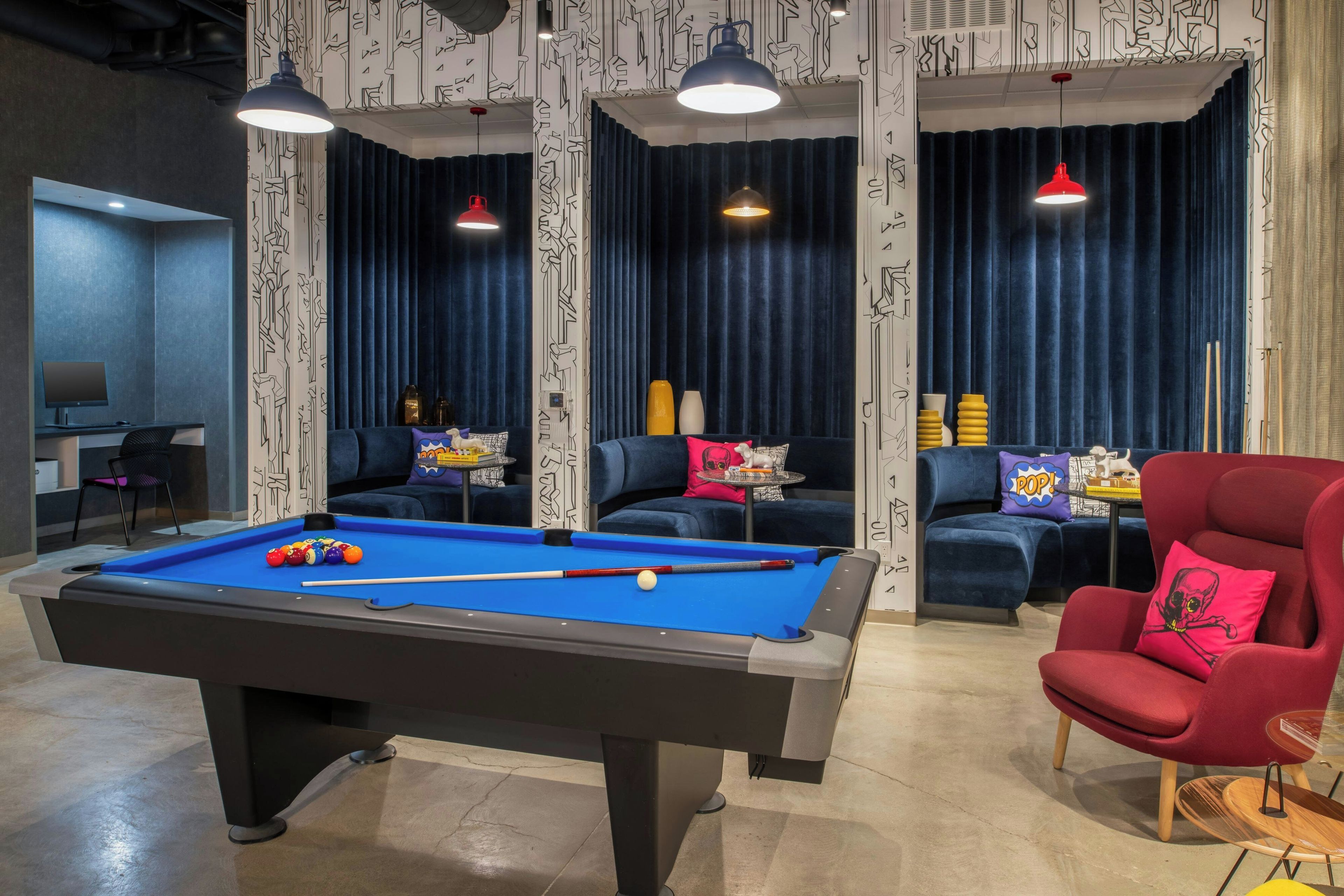 Ein Billardtisch mit Kugeln, ein roter Sessel und eine Couch mit gemusterten Kissen.