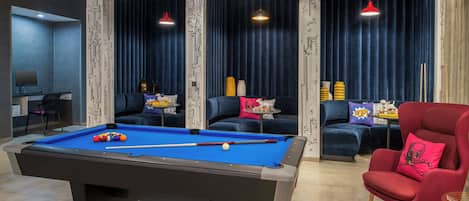 Une table de billard avec des billes, un fauteuil rouge et un canapé avec des coussins à motifs.