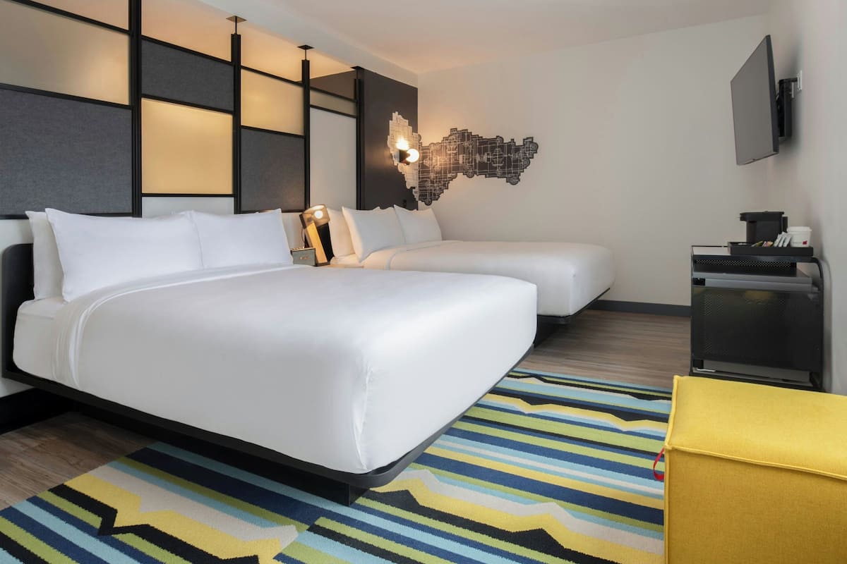 Hotelkamer met een groot bed, een kleiner bed, een bureau met een computer en een televisie aan de muur.