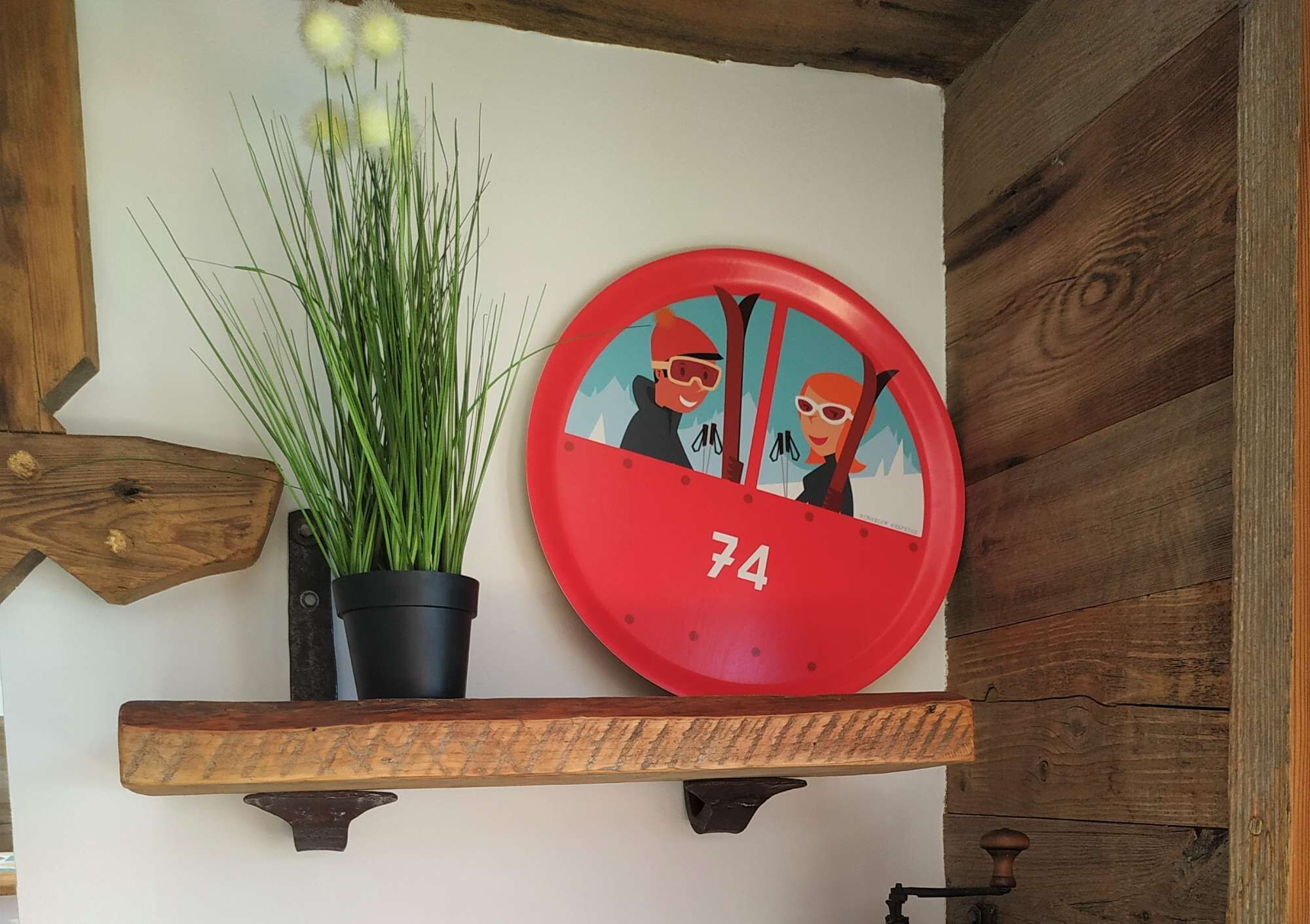 Une horloge murale avec un cadran rouge et le chiffre 74, une plante en pot et des poutres en bois.
