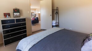 Ein Schlafzimmer mit einem Bett, einer Kommode, einer Tür zu einem Wohnbereich und einem Kleiderständer.