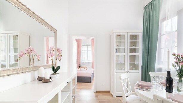 A bright, white bedroom with a large mirror, pink orchids, and a bedside table. - EASY RENT Apartments- OLD TOWN (Lublin)
