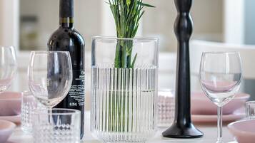 A table with a clear glass vase containing pink flowers, a candle, and a bottle of wine.