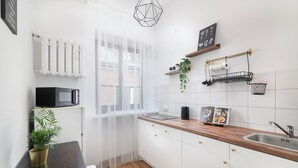 A modern kitchen with white cabinets, a wooden countertop, a black microwave, and a window with sheer curtains. - EASY RENT Apartments- OLD TOWN (Lublin)