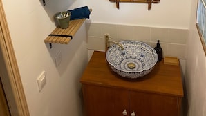 Un baño con tocador de madera, lavabo decorativo, estante de bambú y espejo con marco de bambú.