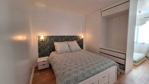 Un dormitorio con cama, mesitas de noche, un armario y una ventana pequeña.