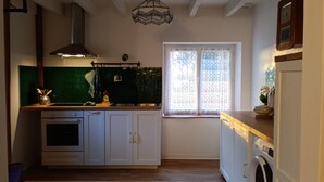 Una cocina con armarios blancos, salpicadero verde, horno empotrado, un lavamanos y una ventana con cortinas estampadas.