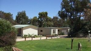 A mobile home with a green roof, a small attached garage, and a grassy yard with benches. - Stawell Caravan Park (Black Range)